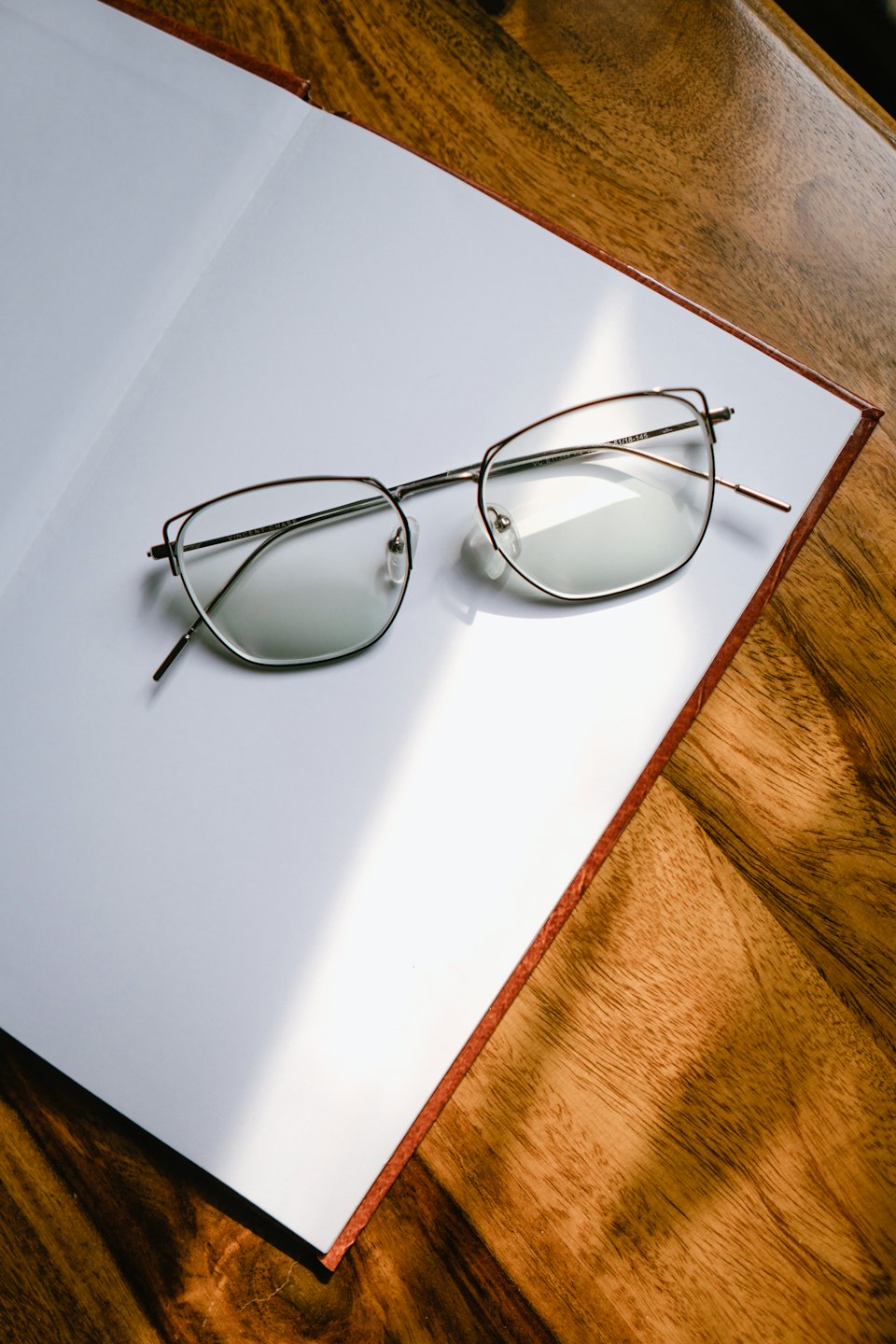 Gafas apoyadas sobre un cuaderno abierto en una mesa de madera.