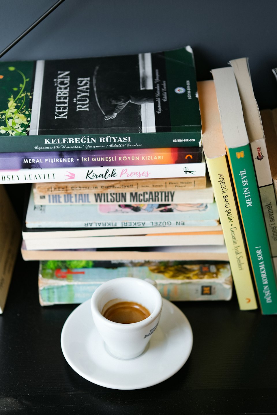 Una taza de espresso sobre un platillo rodeada de libros apilados.